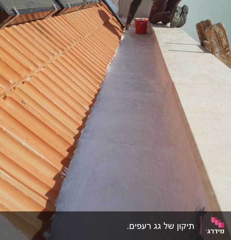 אדם צובע גג עם רעפים אדומים ודלי צבע